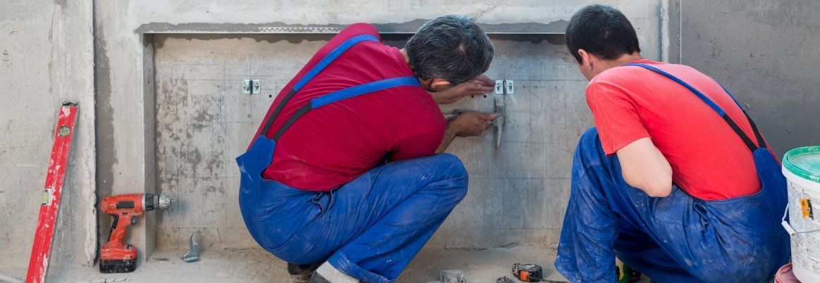 Zwei Handwerker mauern eine Heizungsnische zu.